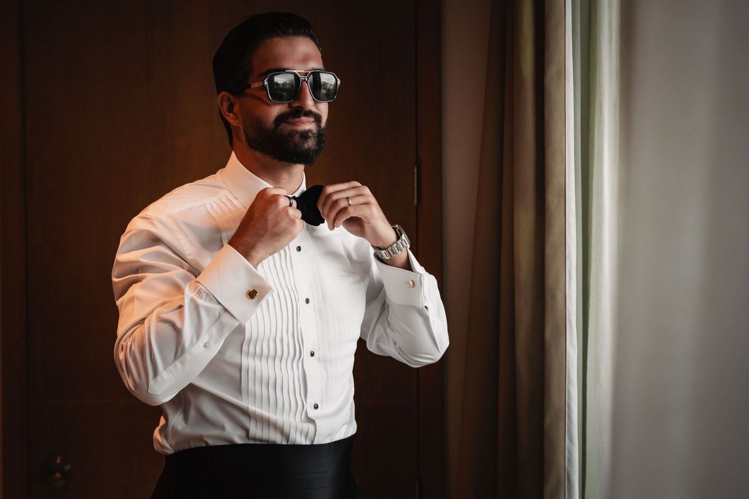 Multiple angles of a groom in formal attire adjusting his bow tie and cuffs.