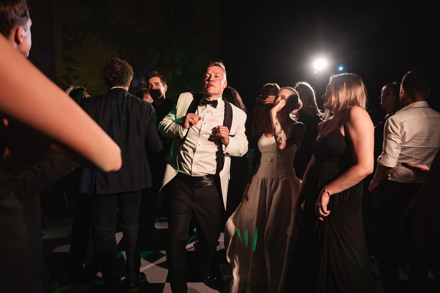 Dark and moody wedding reception dance floor with silhouetted guests and spotlighting.