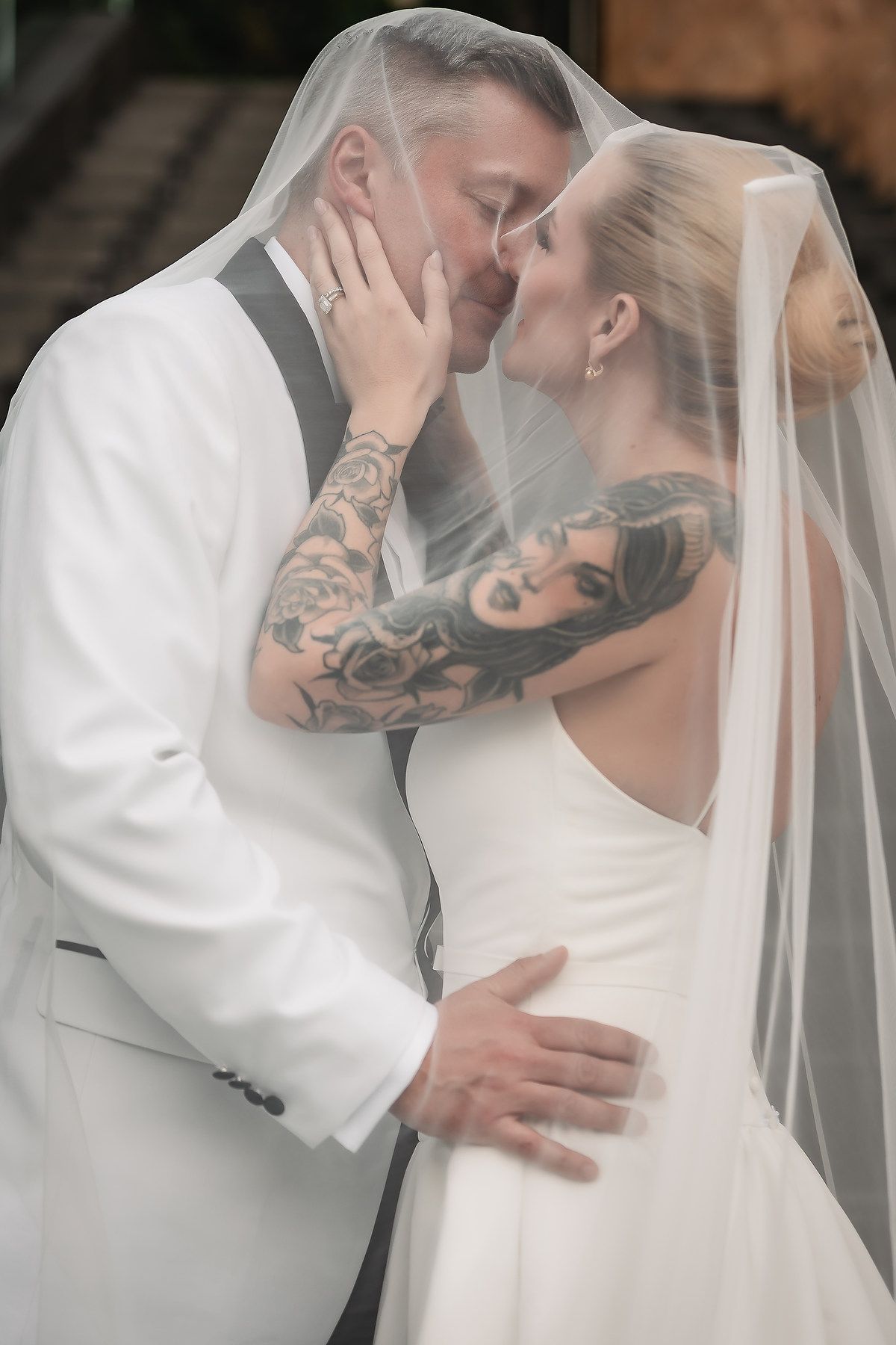 Romantic embrace under sheer wedding veil with visible arm tattoo artwork.