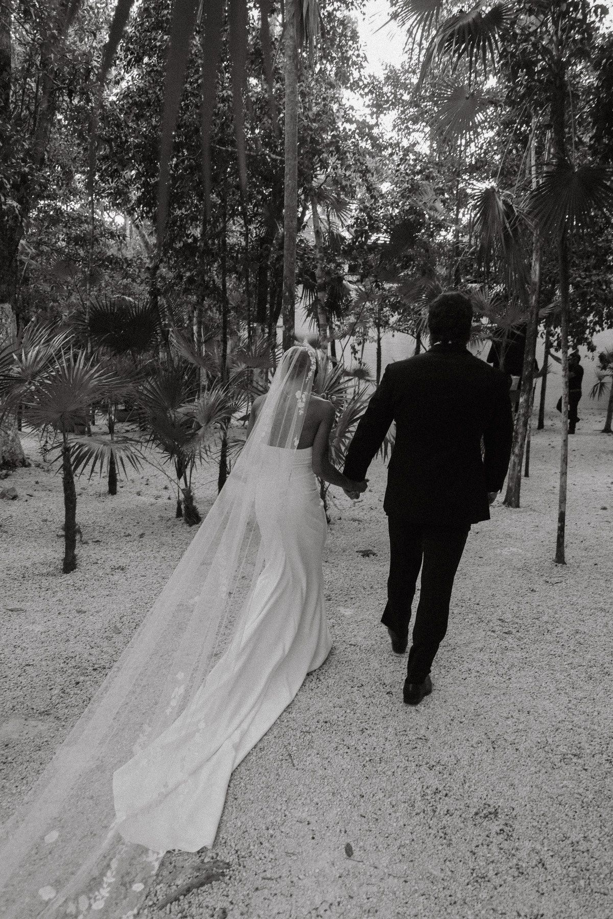Bride and groom walk hand in hand through tropical garden path after outdoor wedding ceremony.