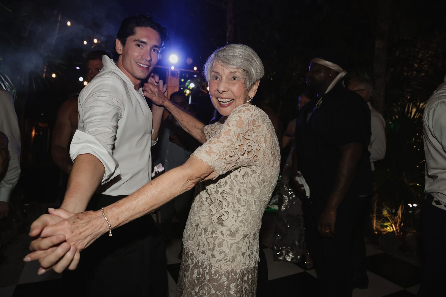 Young man and elderly woman dancing joyfully together at an outdoor evening celebration.