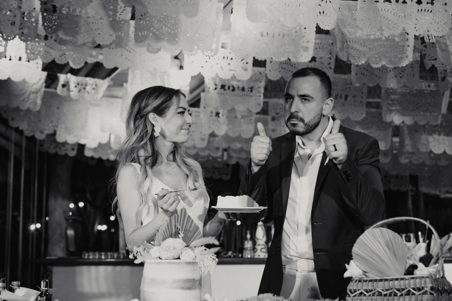 Black and white photo of bride and groom sharing a moment beside wedding cake at reception.