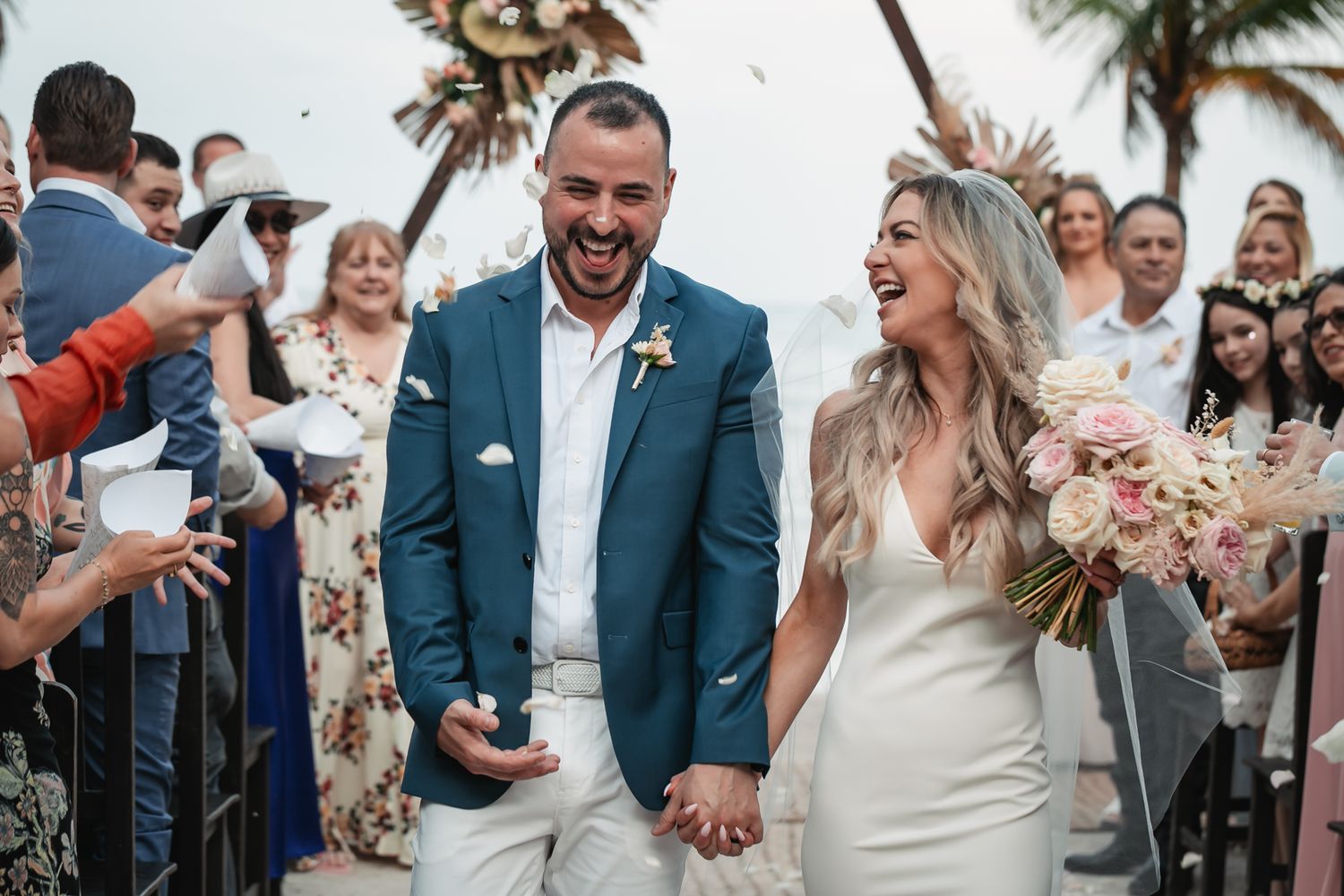 Joyful newlyweds walk down the aisle through a confetti shower at their tropical beach wedding.