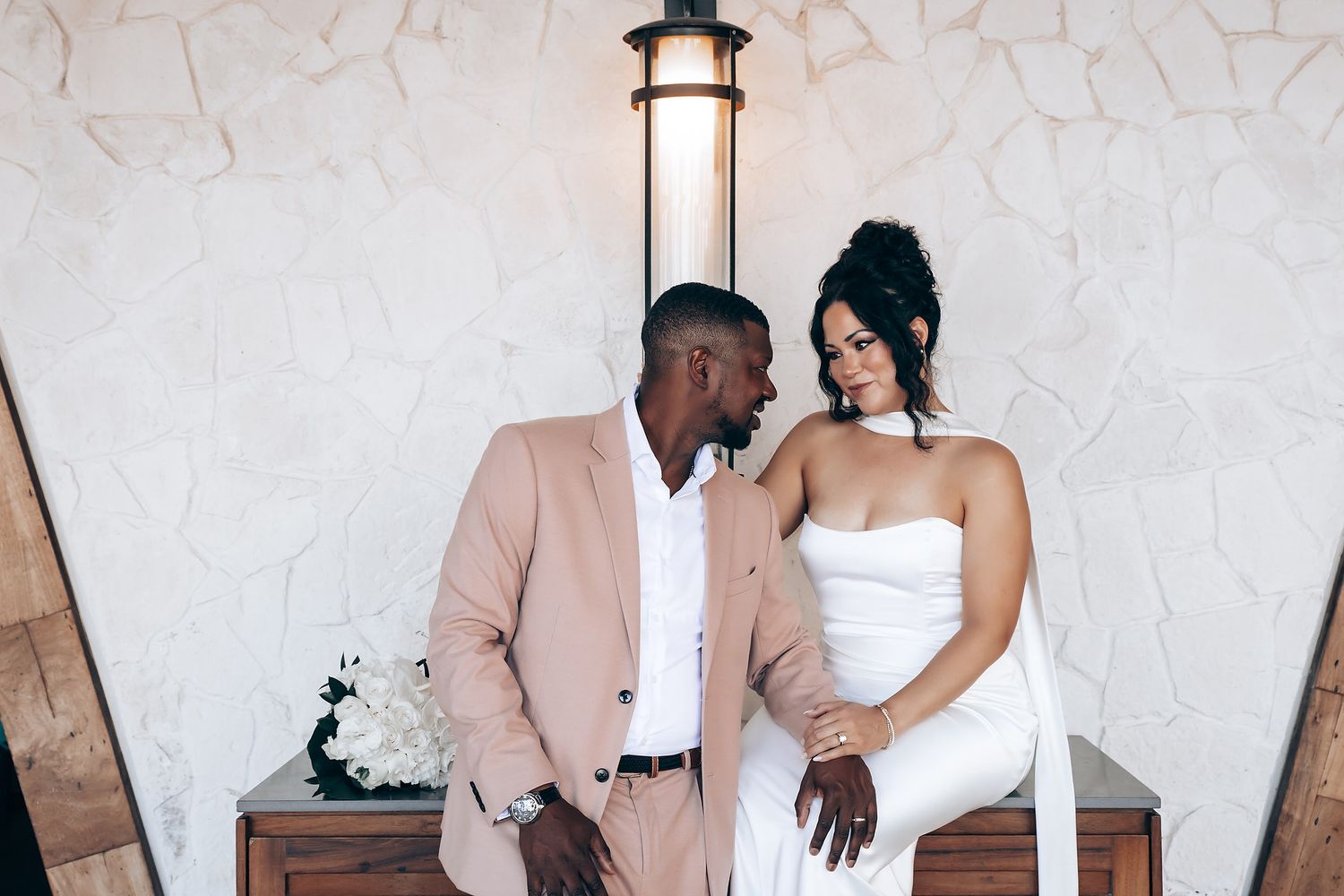 Elegant wedding couple embraces against textured stone wall in romantic photoshoot.