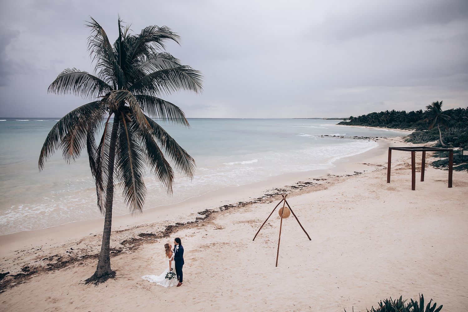 Panoramic beach wedding photography with palm trees and ocean waves in the background.