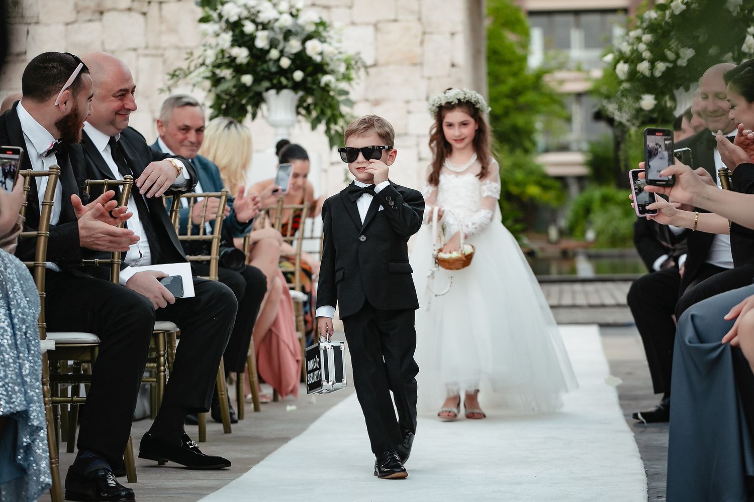 Wedding guests gather outdoors for a celebration at a stone venue with festive decorations and formal attire.