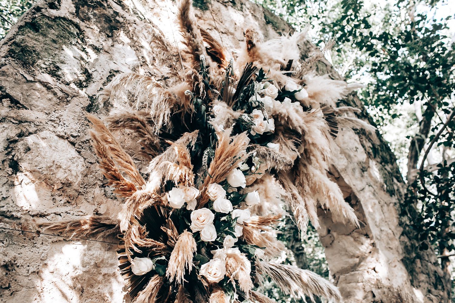 Elegant floral arrangement featuring dried pampas grass and roses in neutral tones against a textured backdrop.
