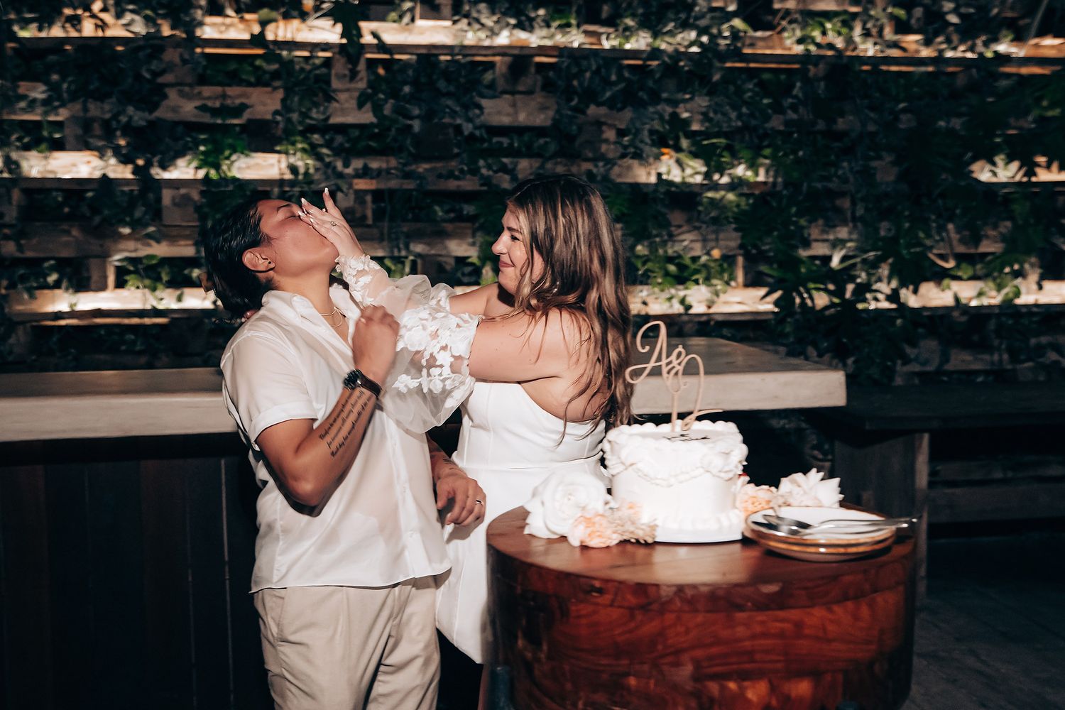 A couple sharing a slice of wedding cake at a rustic wooden table during their reception celebration.