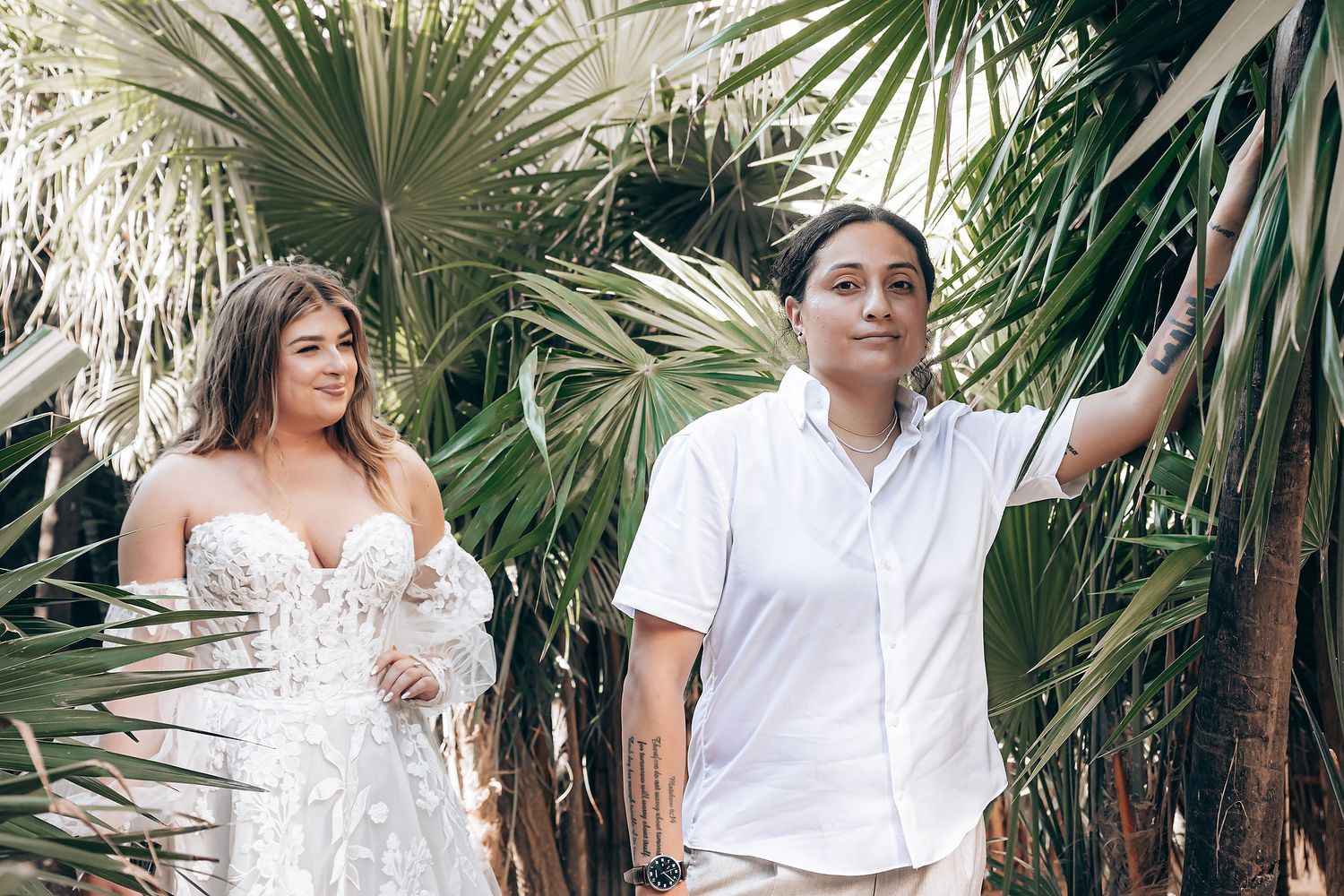 Couple in white outfits poses together among tropical palm trees for romantic outdoor photo session.