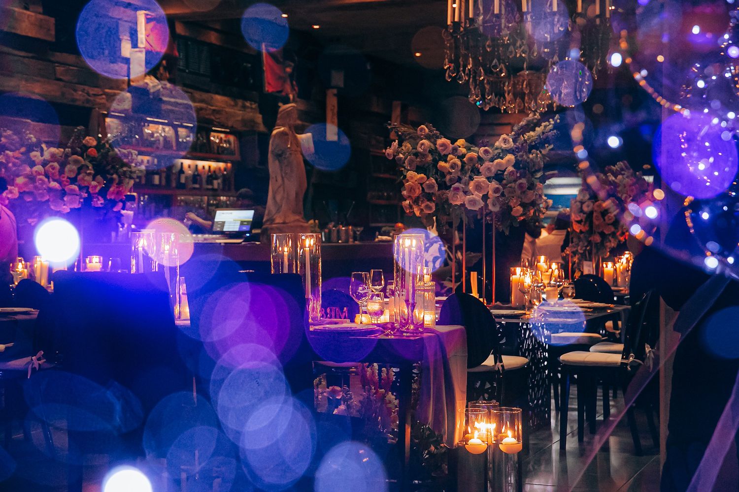 Elegant restaurant interior with moody purple lighting, crystal chandeliers, and candlelit tables creating a romantic atmosphere.