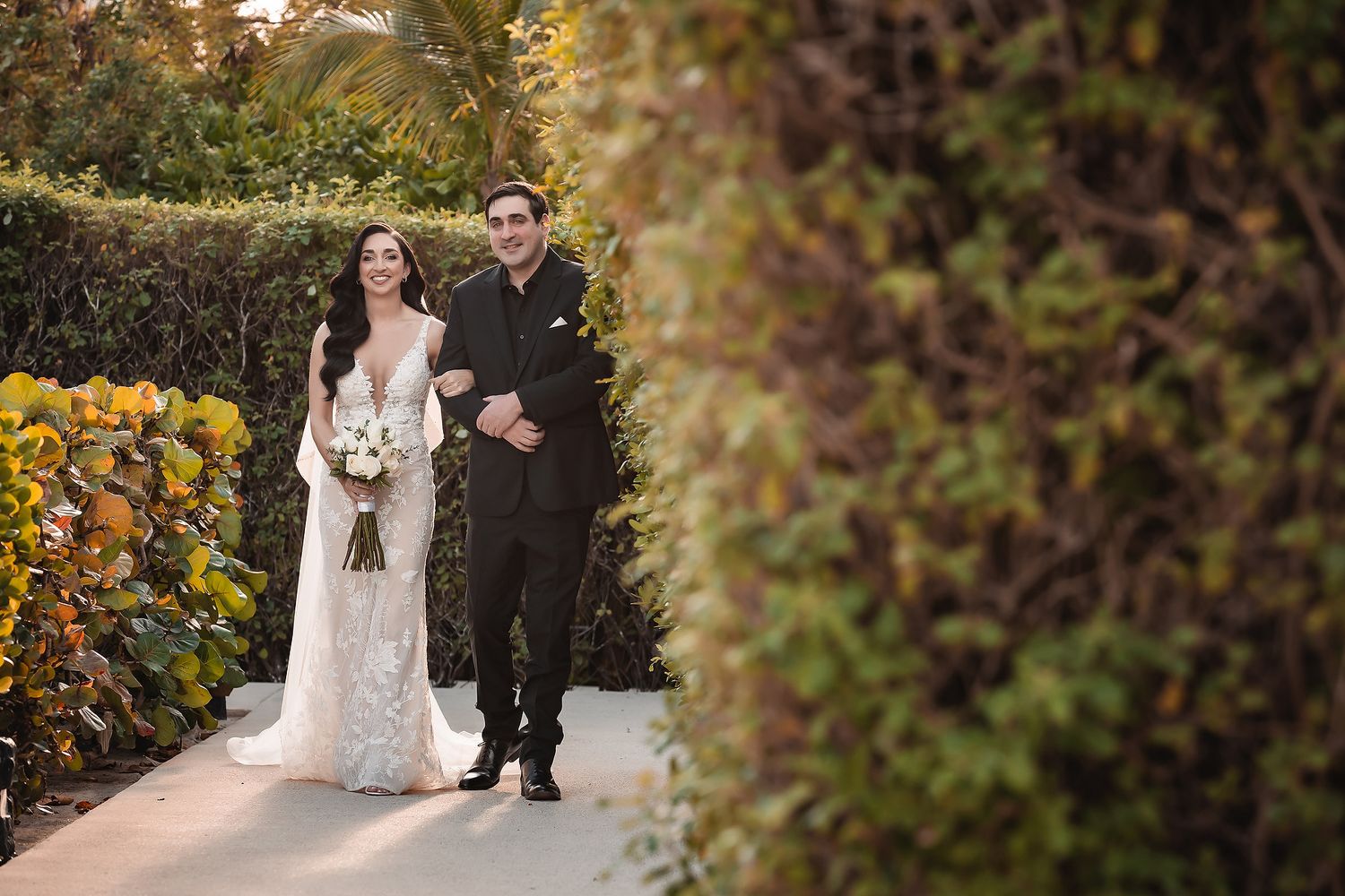 Newlyweds share an intimate moment while walking through a garden path with autumn foliage.