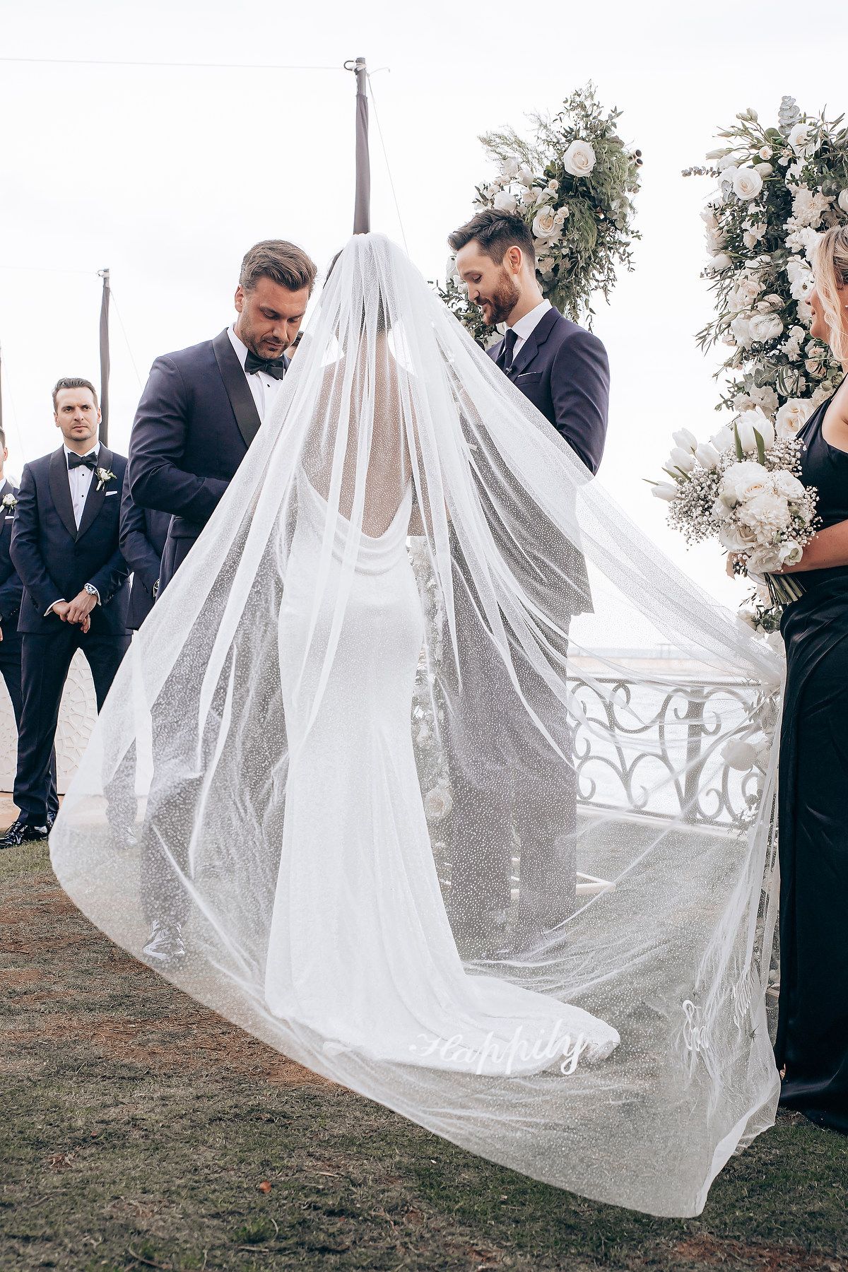 Outdoor wedding ceremony under floral arch with guests watching the celebration.