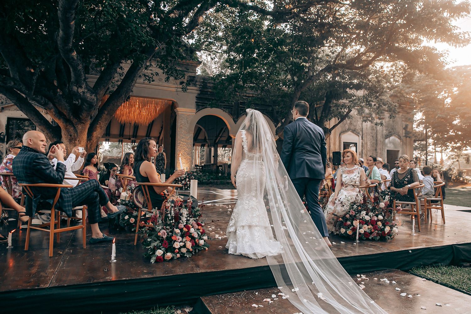 Elegant beach wedding ceremony with white chairs and floral decorations at sunset.