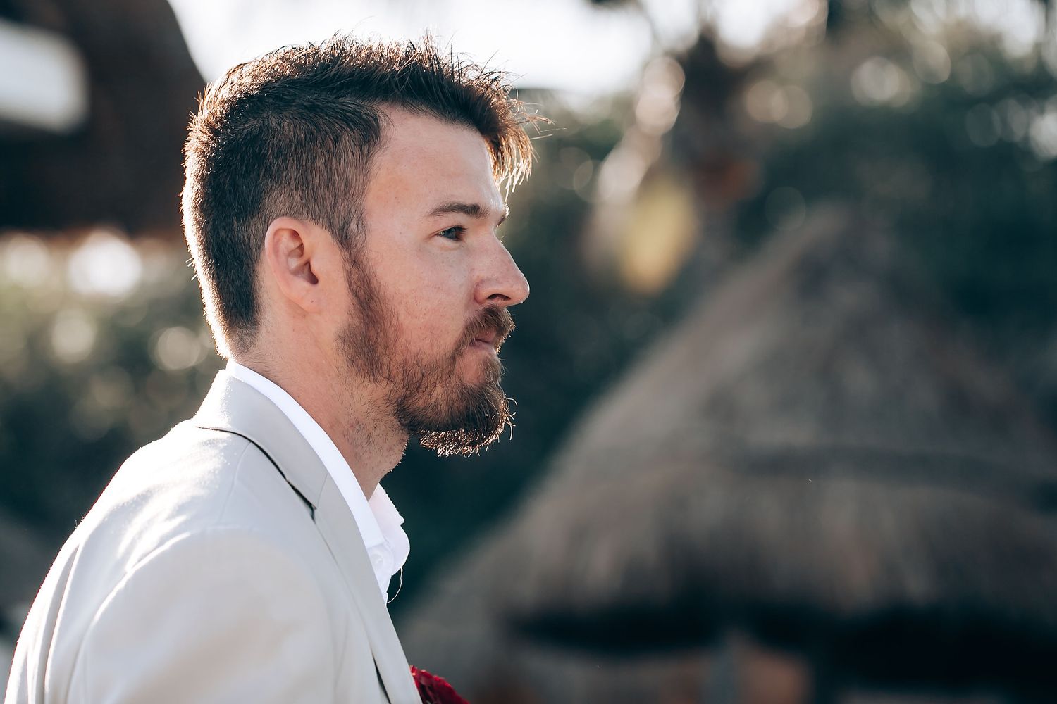 A groom in a white dress shirt and beard stands during an outdoor wedding ceremony.