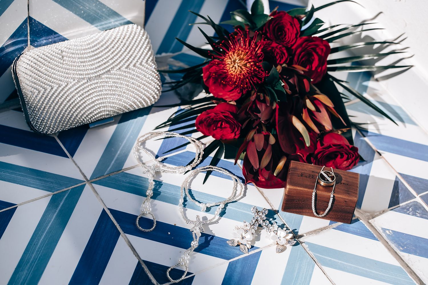 A red floral bouquet sits beside a white clutch on blue and white geometric patterned tiles.