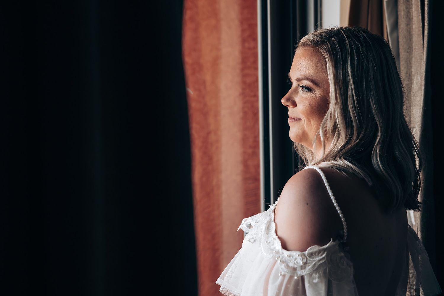 Natural light portraits of bride by window in elegant white dress.