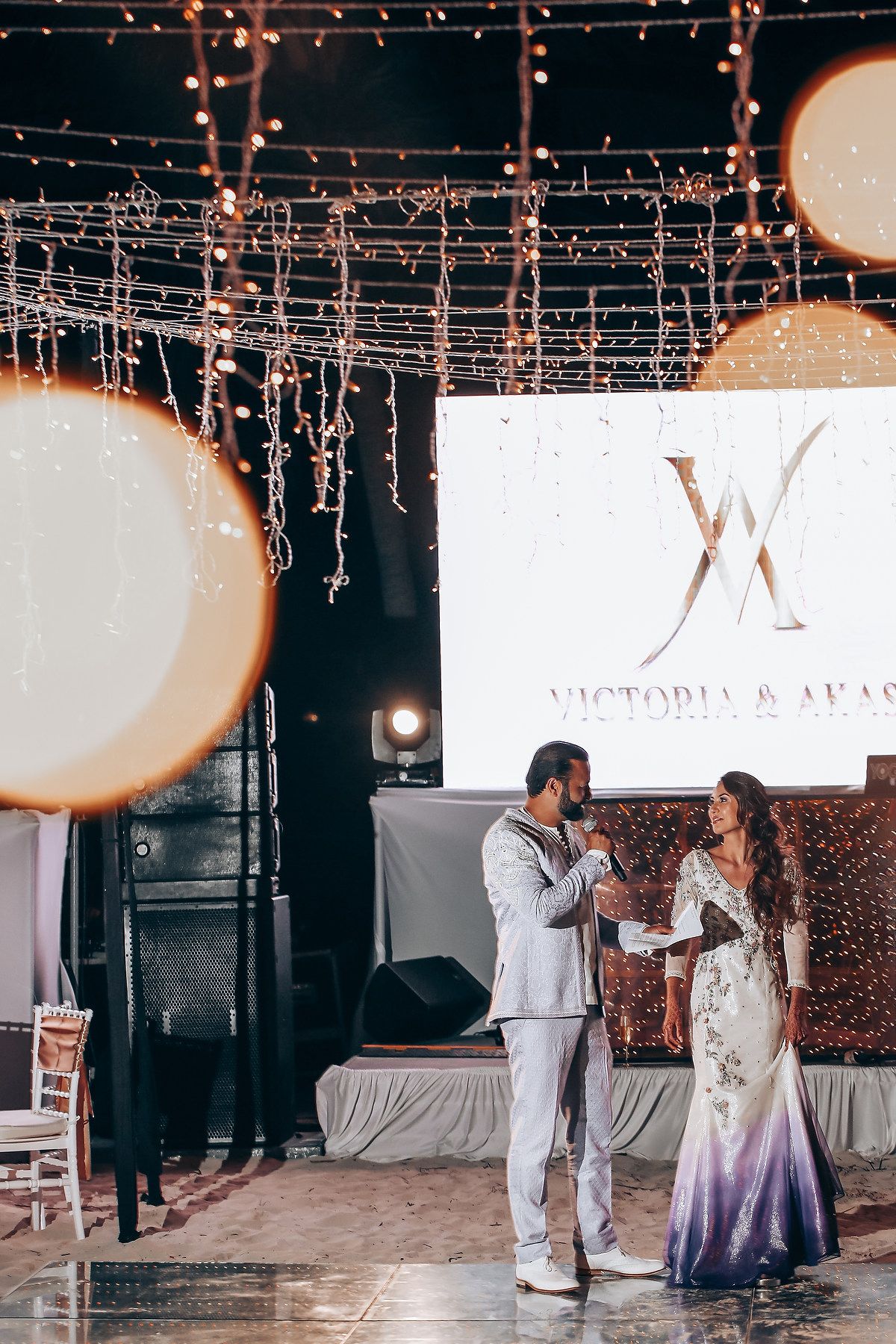 Couple dancing together under twinkling string lights at an indoor reception venue.