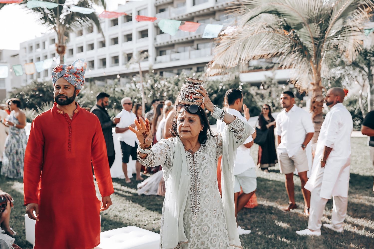 Wedding guests dancing and celebrating at an outdoor reception with palm trees and buildings in the background.