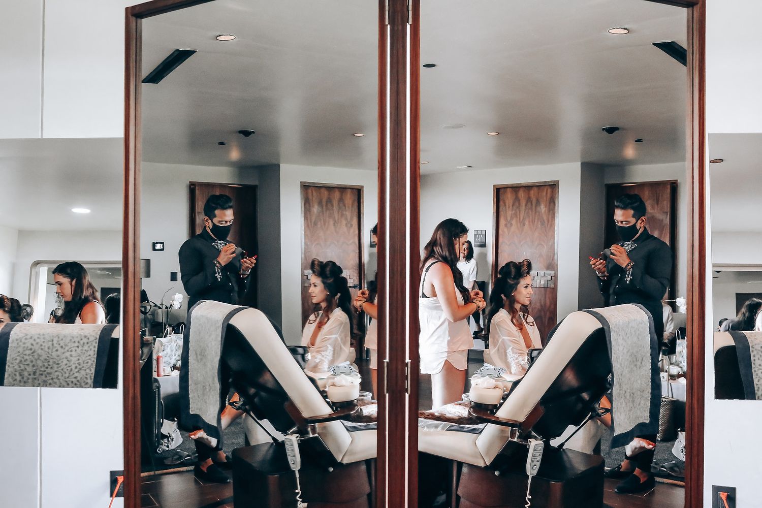 Mirrored reflection shows a beauty salon interior with styling chairs and people during a hair appointment.