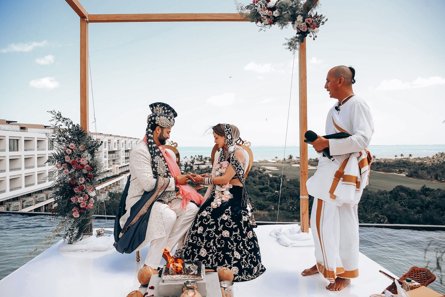 Wedding guests gathered outdoors under blue sky for seaside celebration with tropical decor.