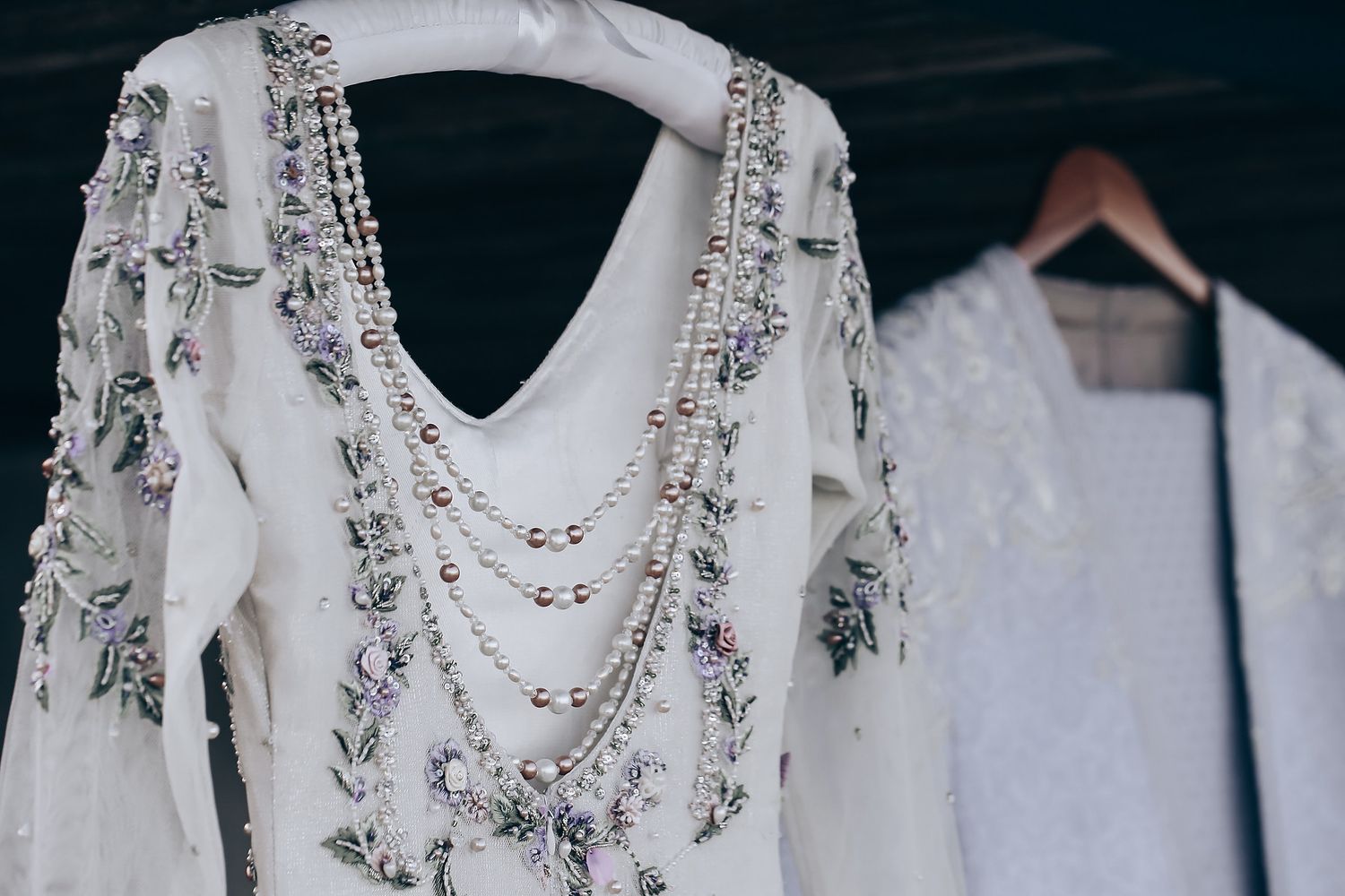 Row of elegant white wedding dresses hanging on hangers against dark background.