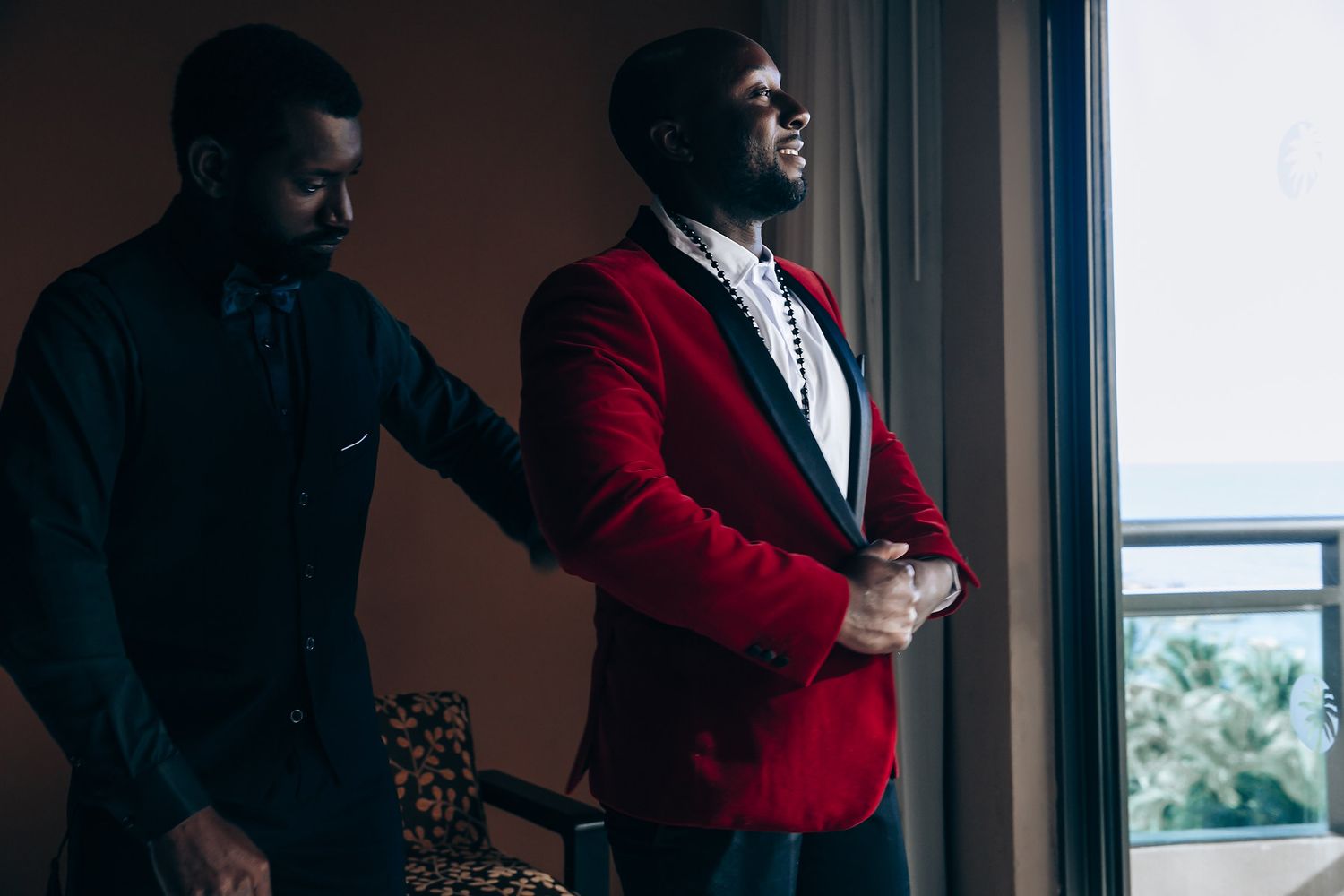 Couple in contrasting white and red outfits pose by window in moody indoor photoshoot setting.