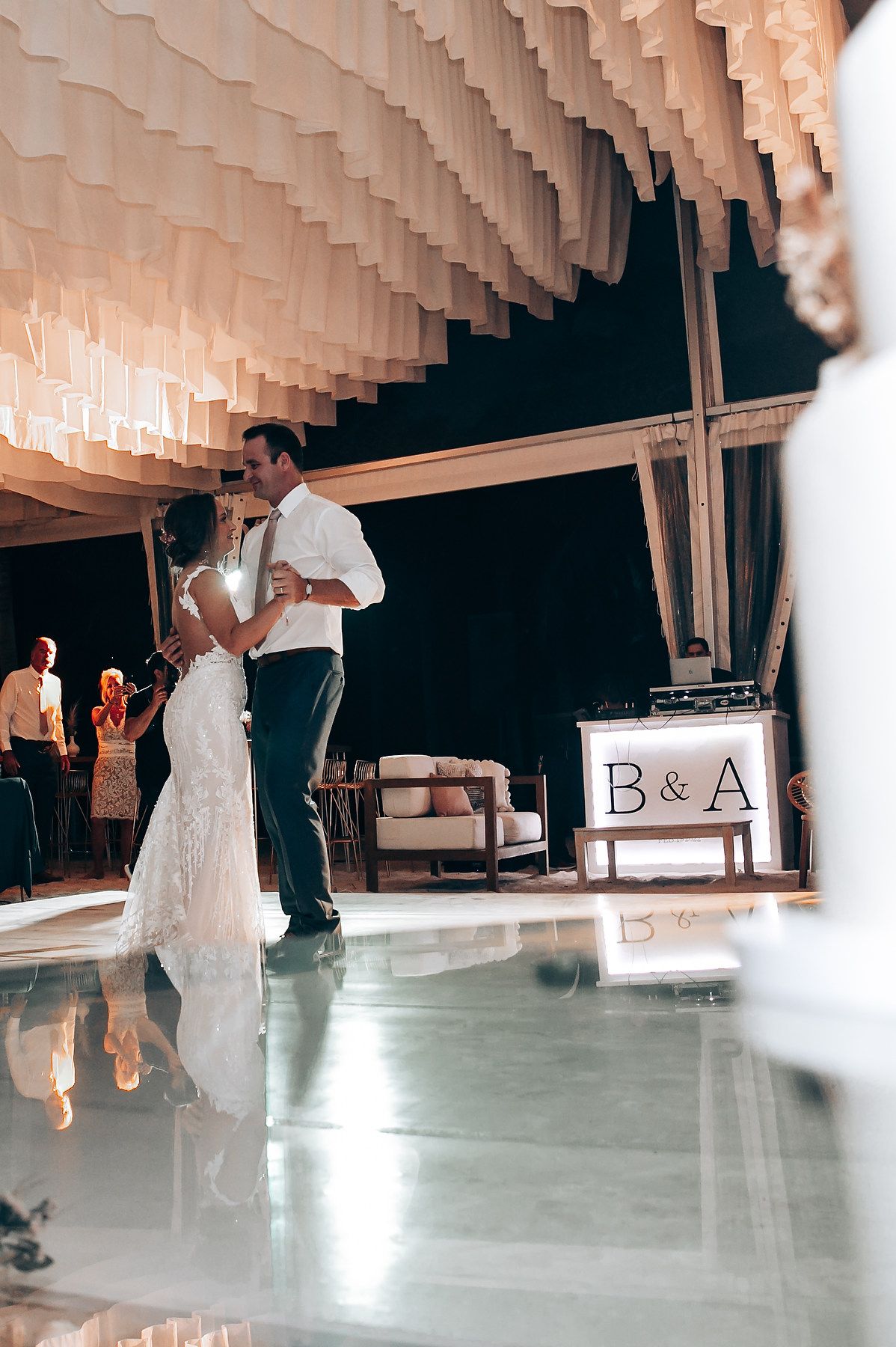 Wedding reception dance floor with elegant white draped ceiling and monogram lighting.