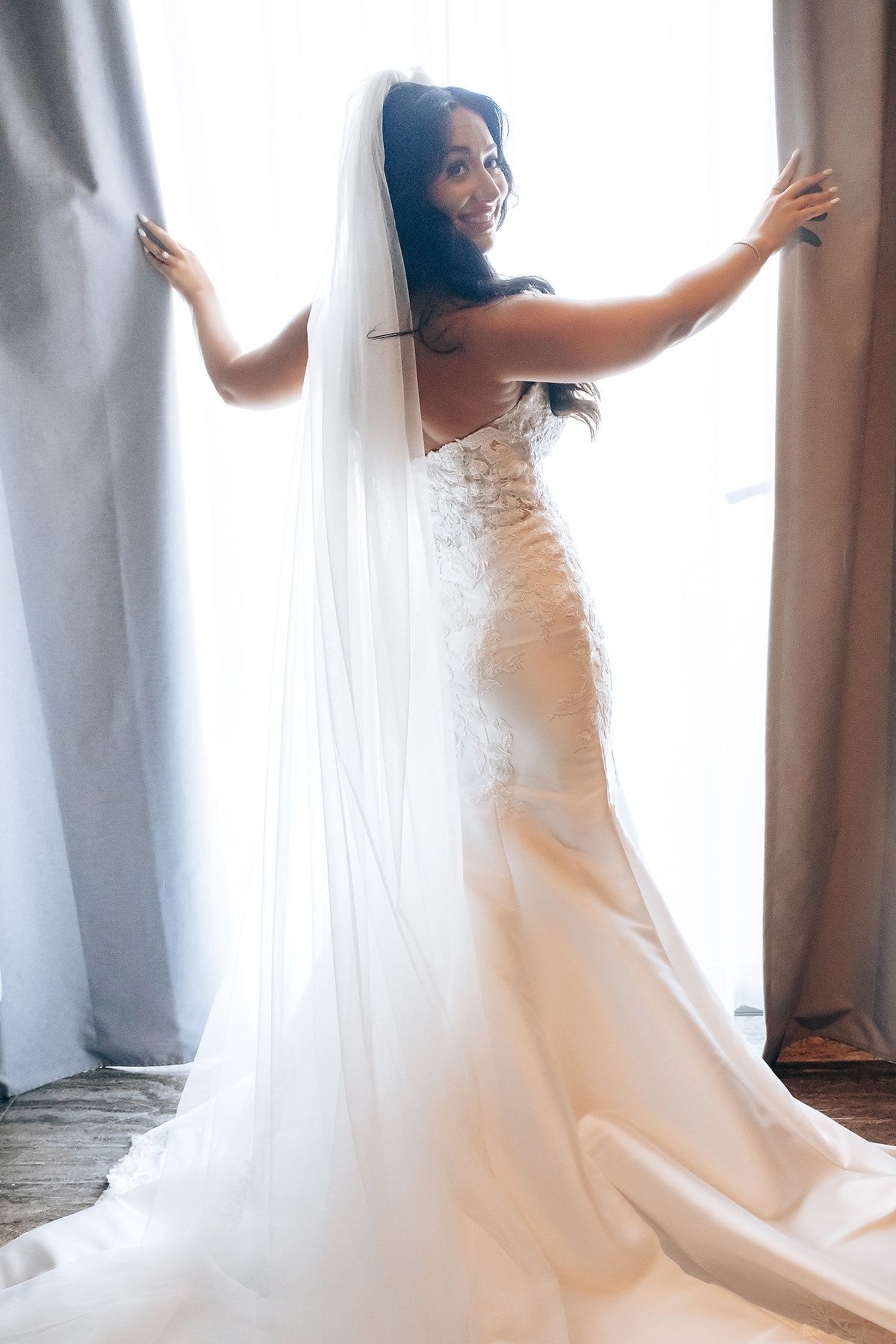 A stunning mermaid style wedding dress with intricate lace details and flowing train captured in natural window light.