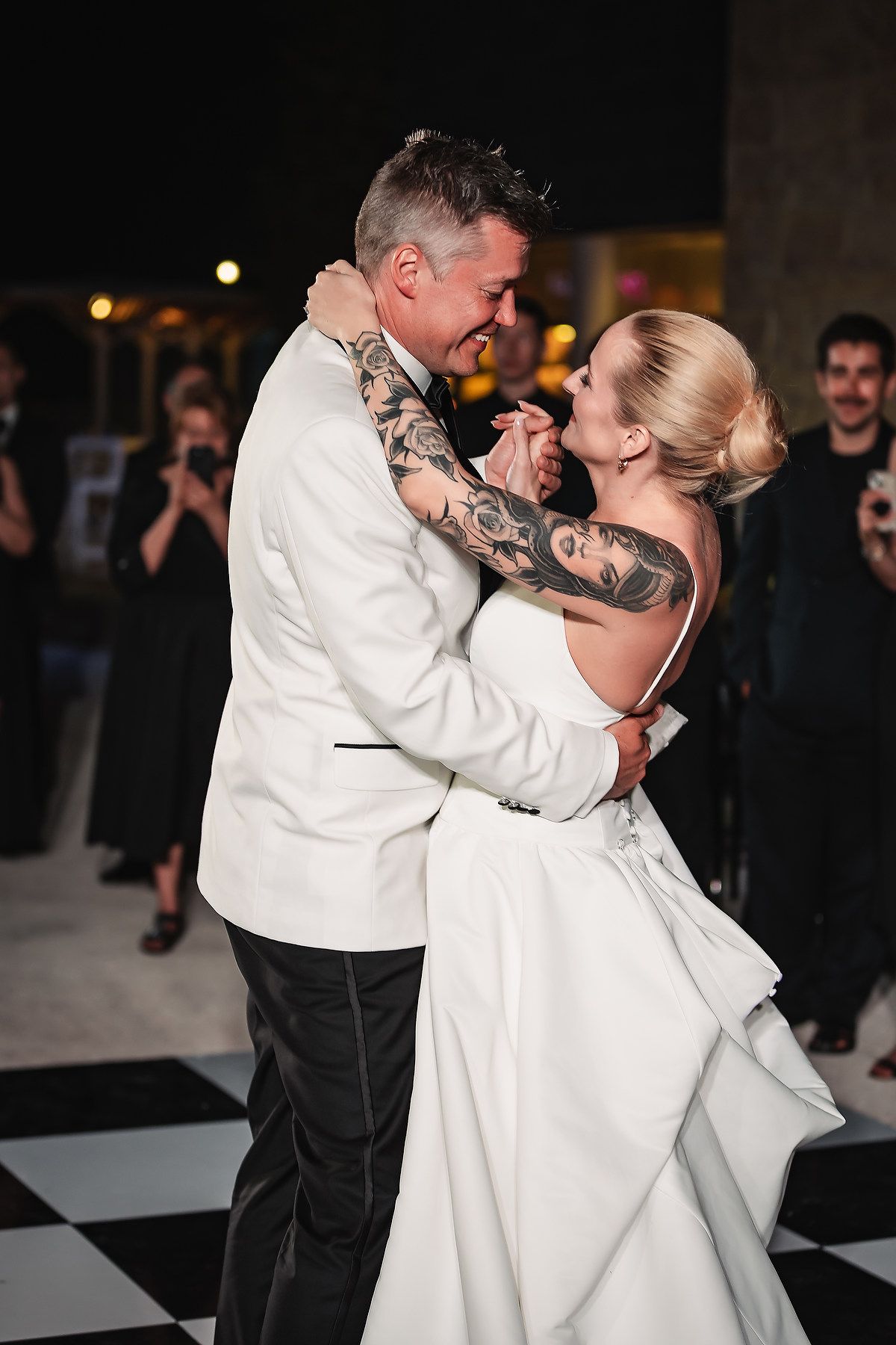 A couple shares a romantic dance at their wedding reception on a black and white dance floor.