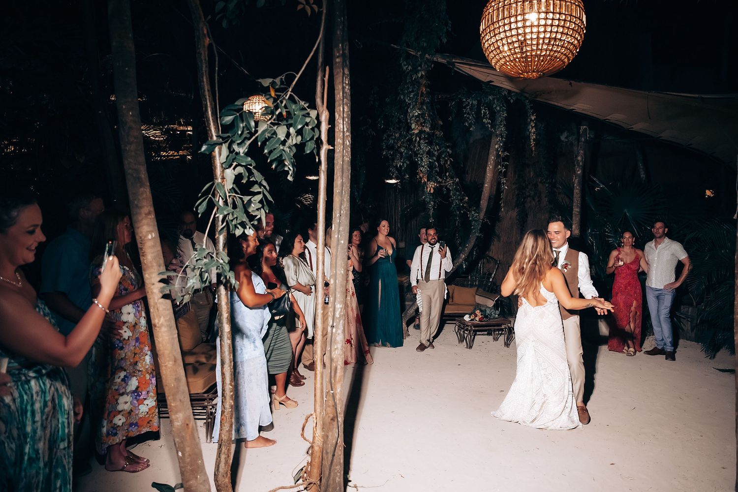 Disco ball illuminates a dark dance floor at a wedding reception with guests dancing in the background.