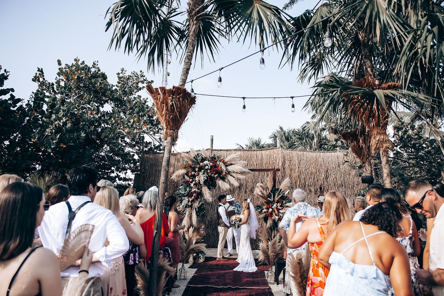 Outdoor wedding ceremony setup with palm trees and pampas grass decorations.