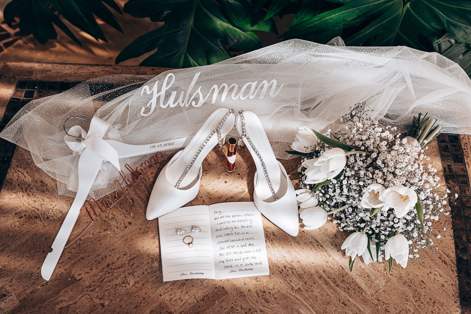Wedding detail flat lay with veil, heels, invitation and white floral bouquet.