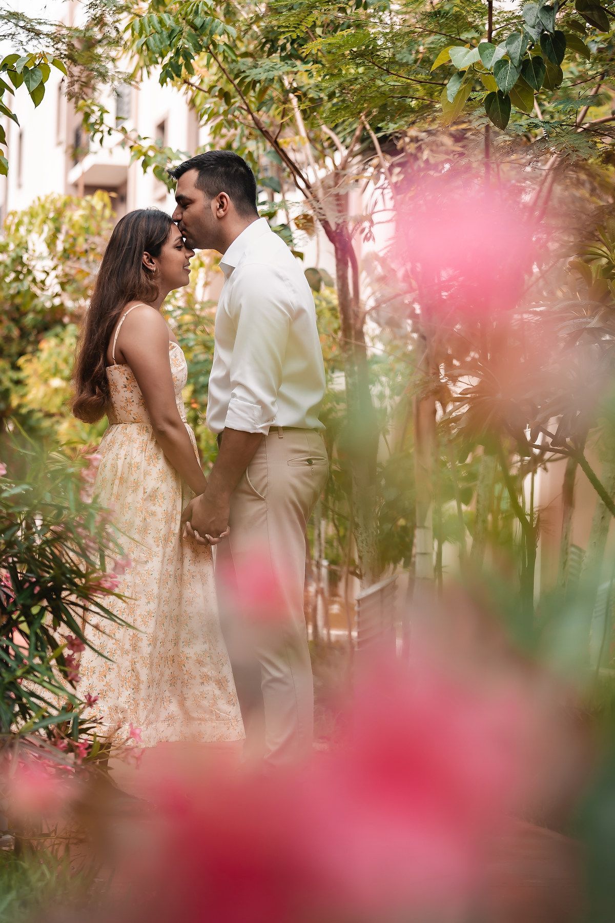 Romantic photoshoot through pink flowers and greenery in a garden setting.