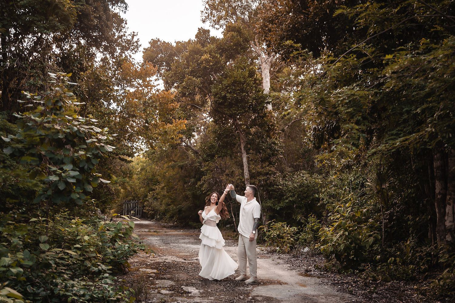 A couple in coordinated white outfits explores a serene woodland setting.