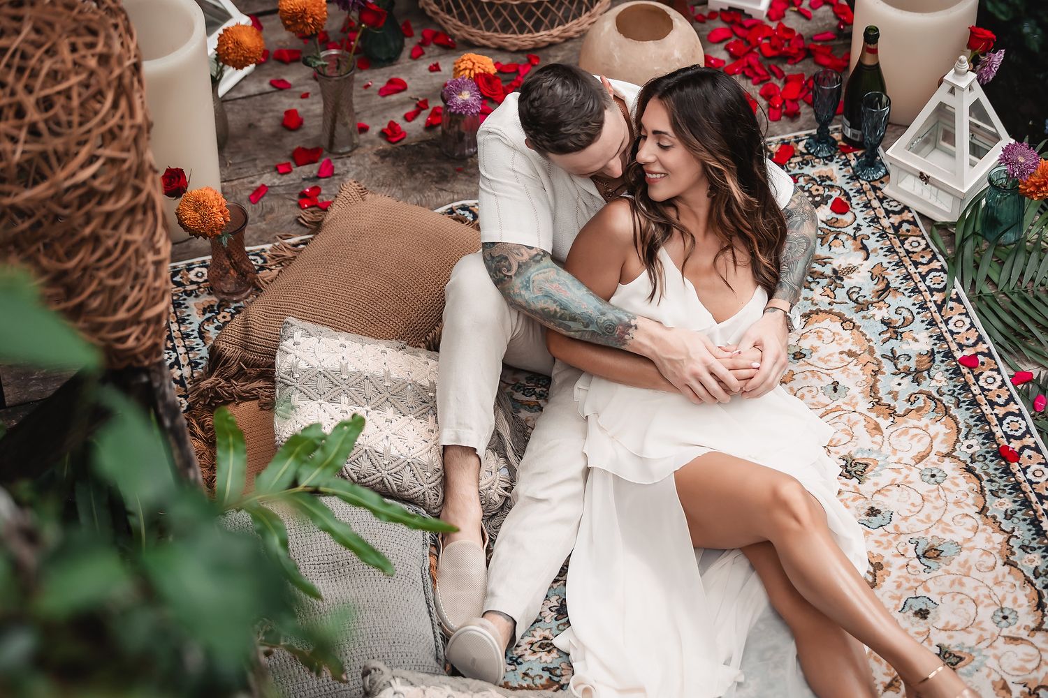 Intimate moment captured on decorative blanket surrounded by lanterns and rose petals.