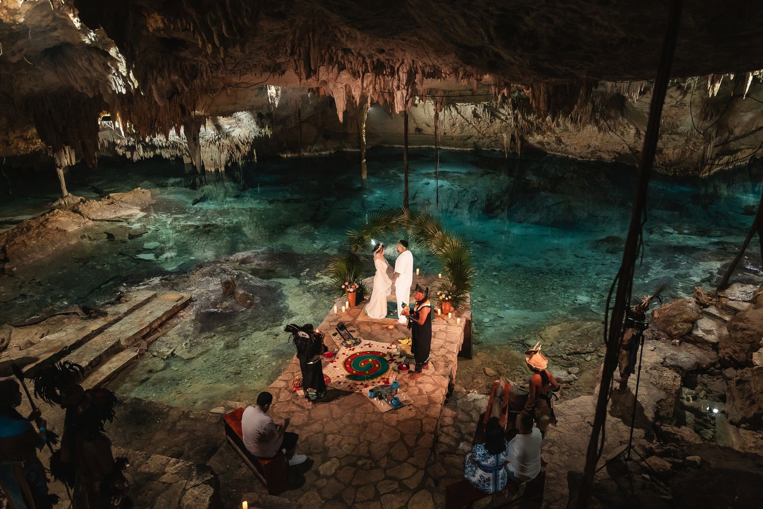 A romantic wedding ceremony setup in a stunning cave cenote with turquoise water and ambient lighting.