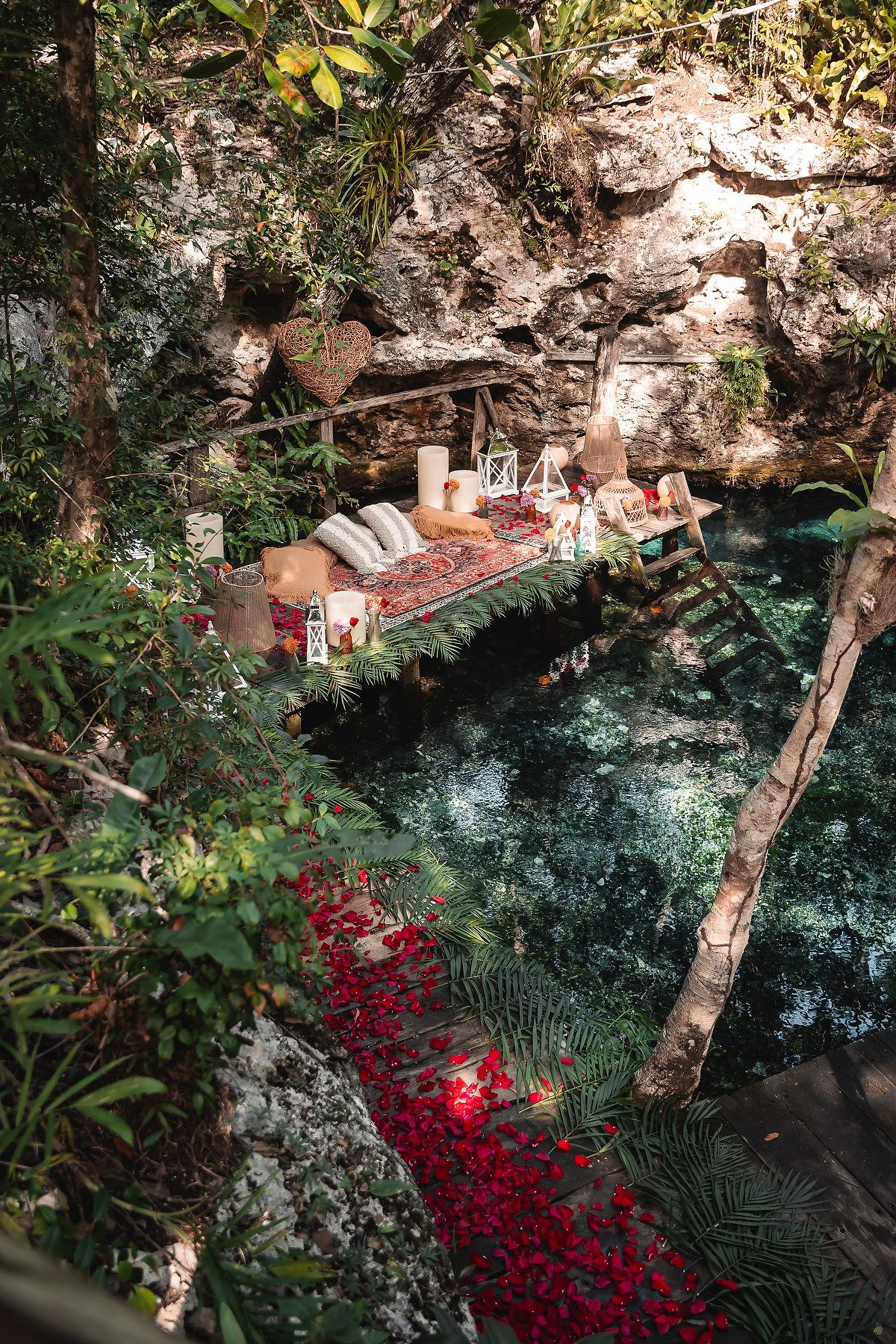 Bohemian style picnic setup with lanterns and cushions beside a natural turquoise pool.