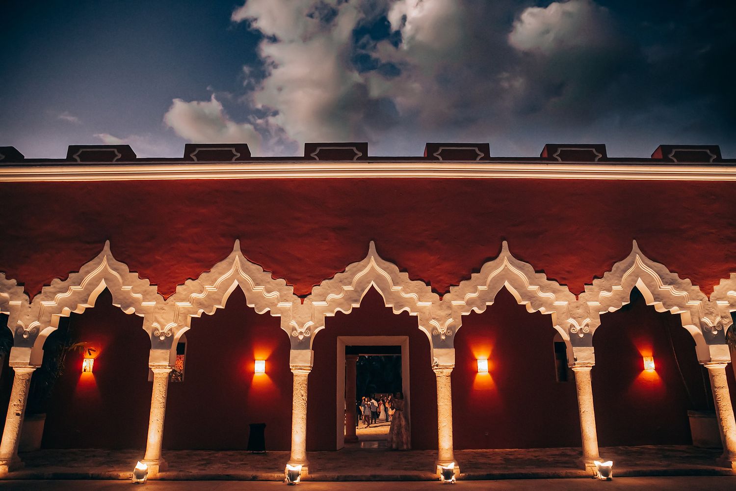 Ornate architectural details of a traditional Asian temple roof with red lanterns illuminated at night against a dark sky.