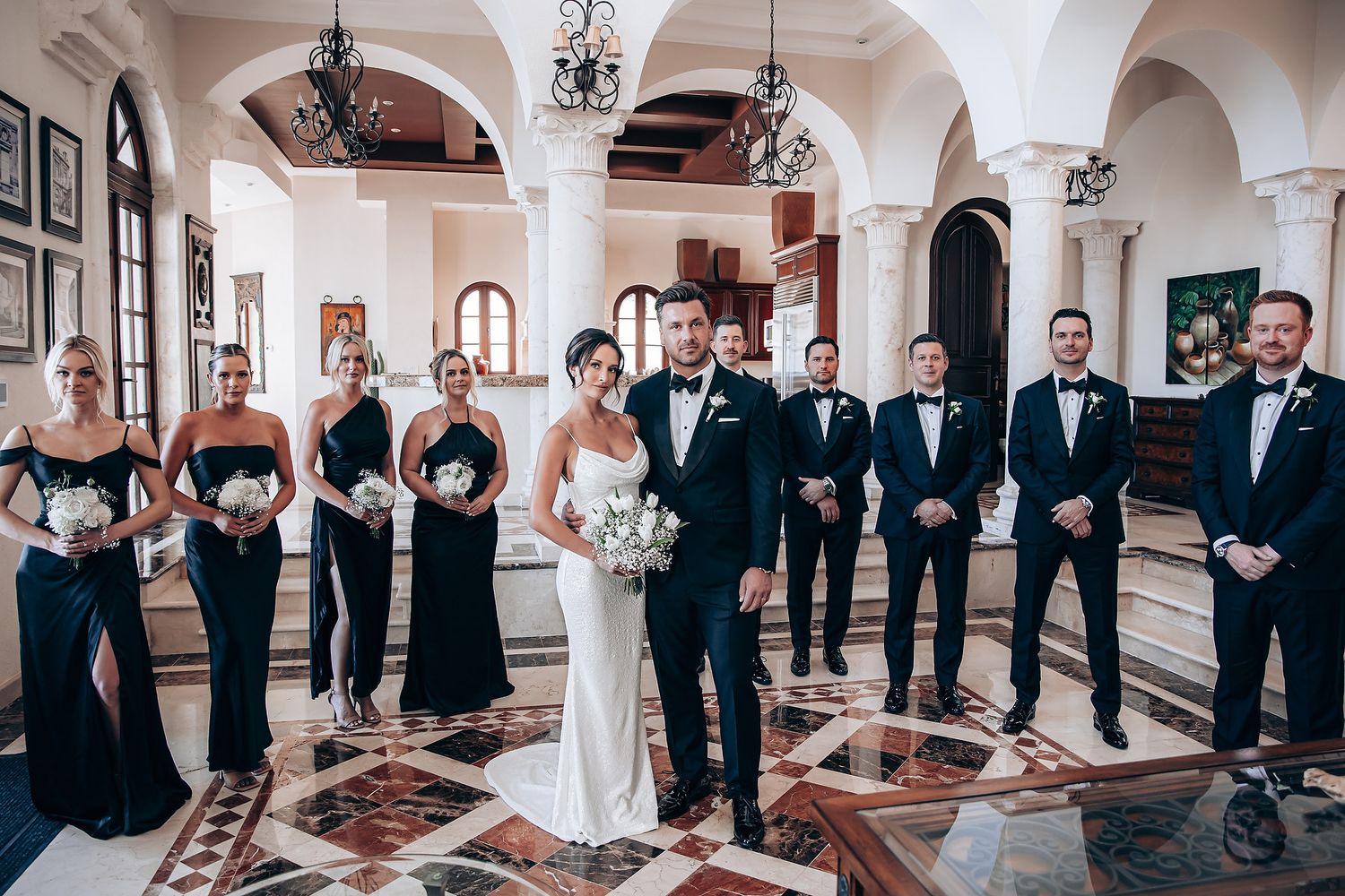 A panoramic view of a wedding ceremony in a grand hall with arched columns and chandeliers.