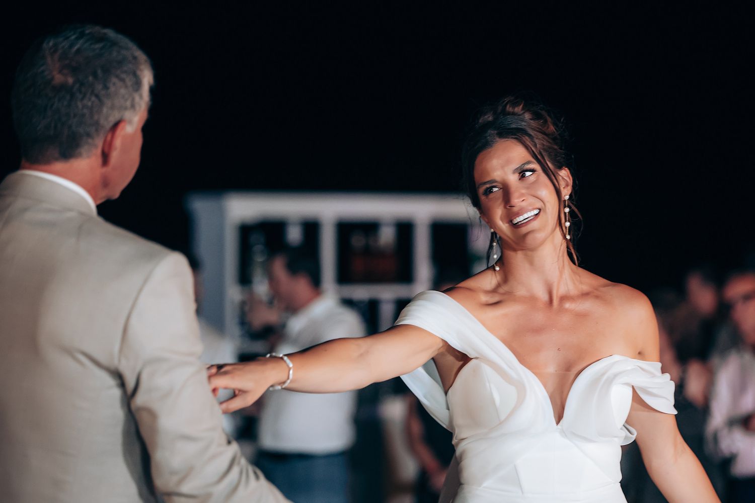 A bride and groom share their first dance at an elegant indoor wedding reception while guests look on.