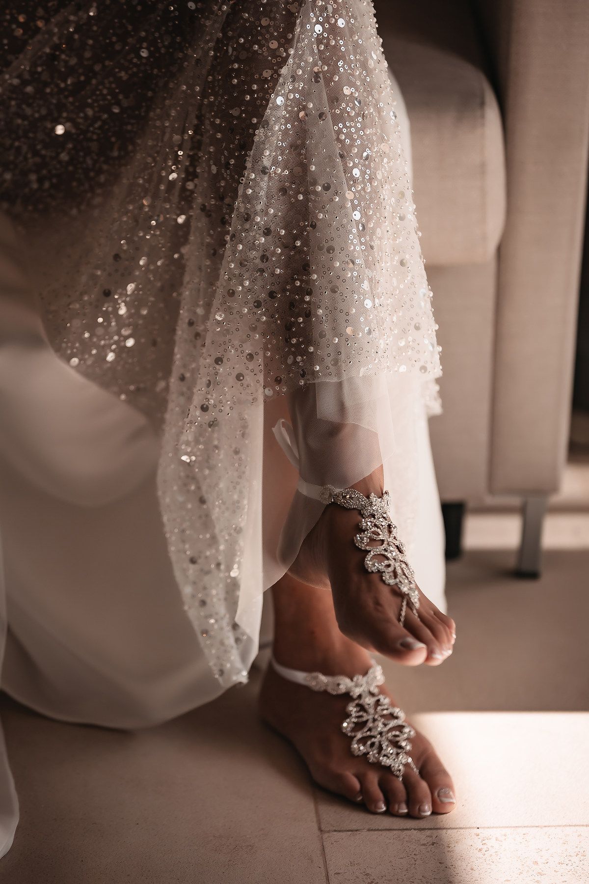 Close-up details of sparkly bridal accessories and anklet jewelry against a white wedding dress.