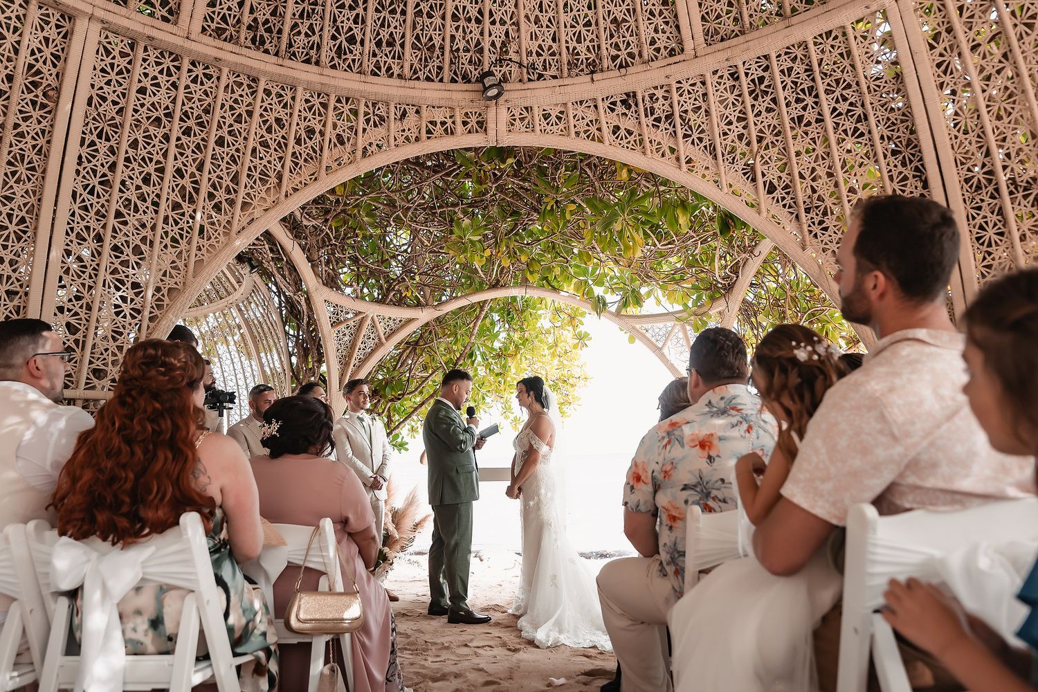 Wedding party and guests dancing under a beautifully lit latticed pavilion structure.