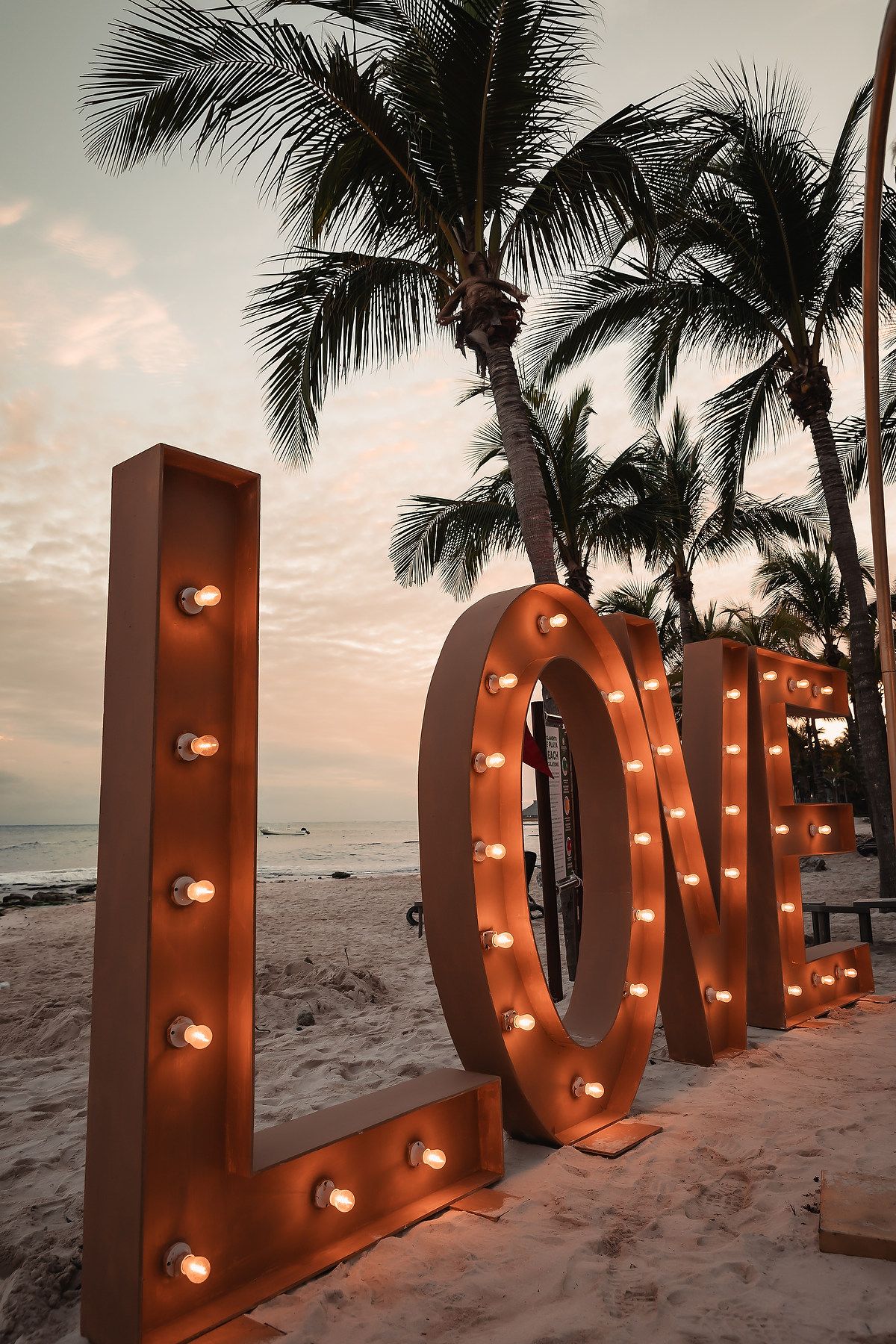 Illuminated LOVE letters on a sandy beach at sunset with palm trees in the background.