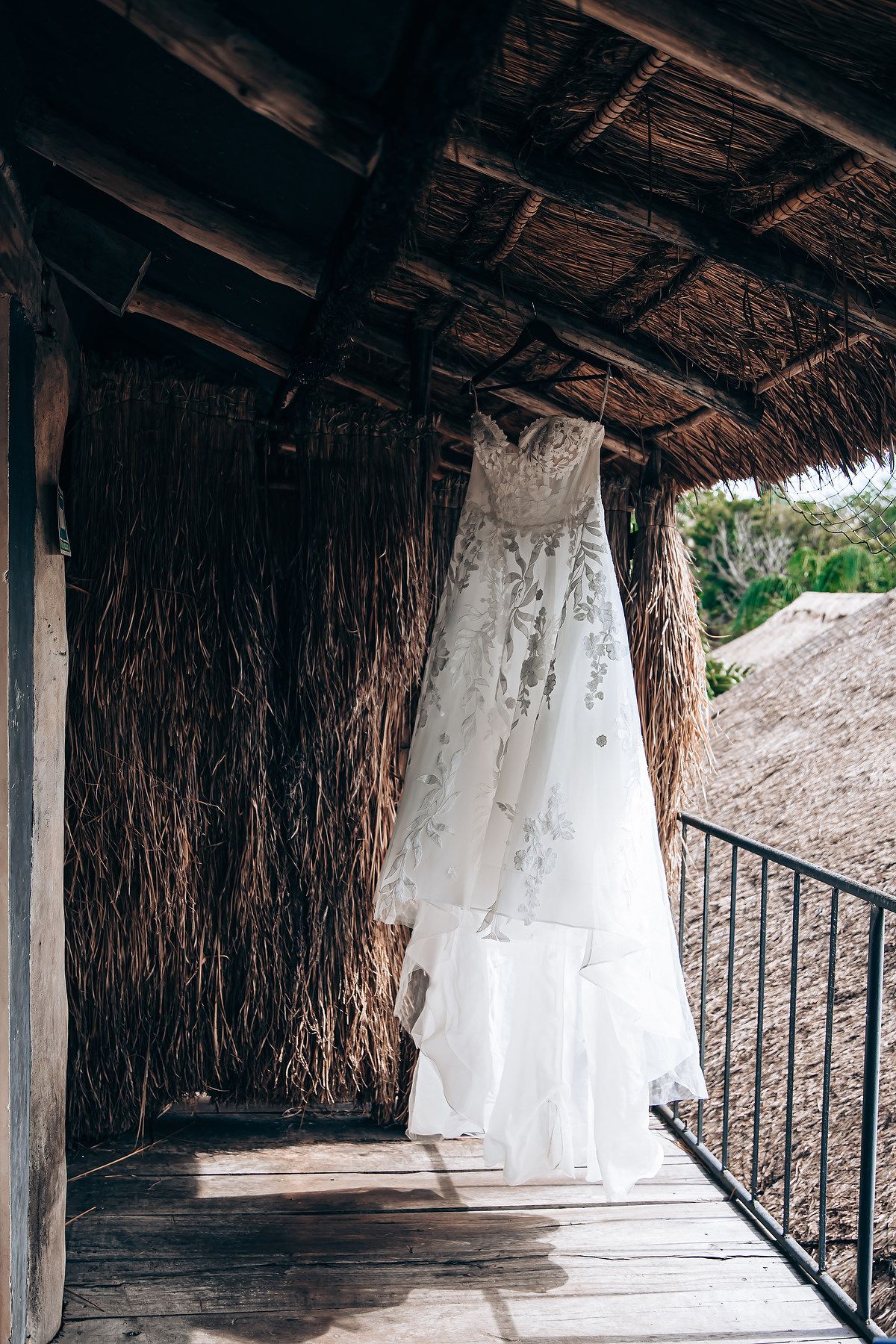 White wedding dresses hanging in a rustic thatched roof pavilion.