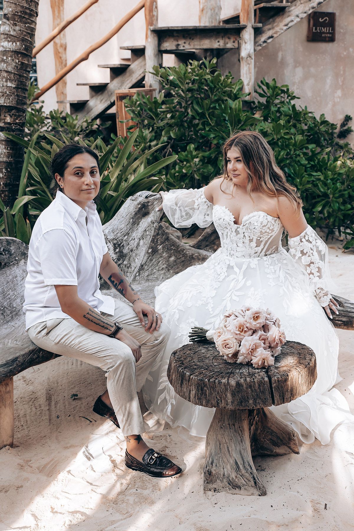 A couple poses on a rustic wooden stump seat during their beach wedding photoshoot.