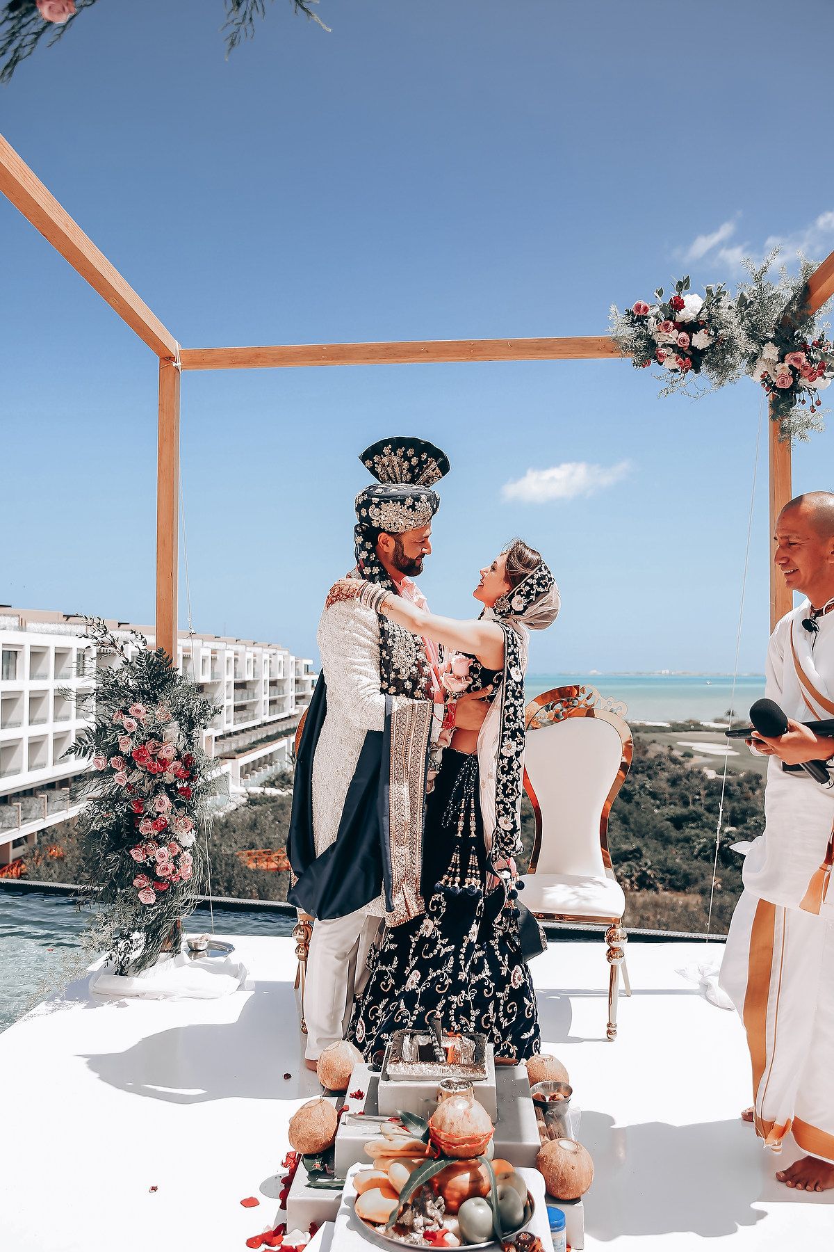 A wedding ceremony setup on a white terrace overlooking the ocean with wooden posts and floral decor.
