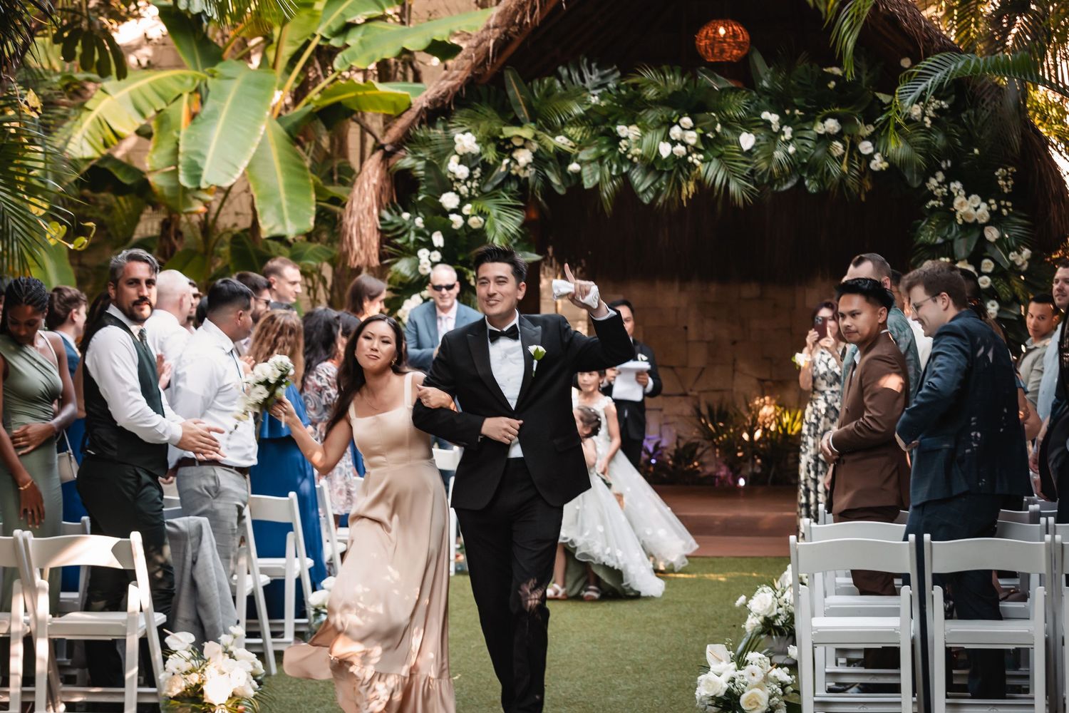 Outdoor wedding ceremony setup with white chairs and tropical garden backdrop.