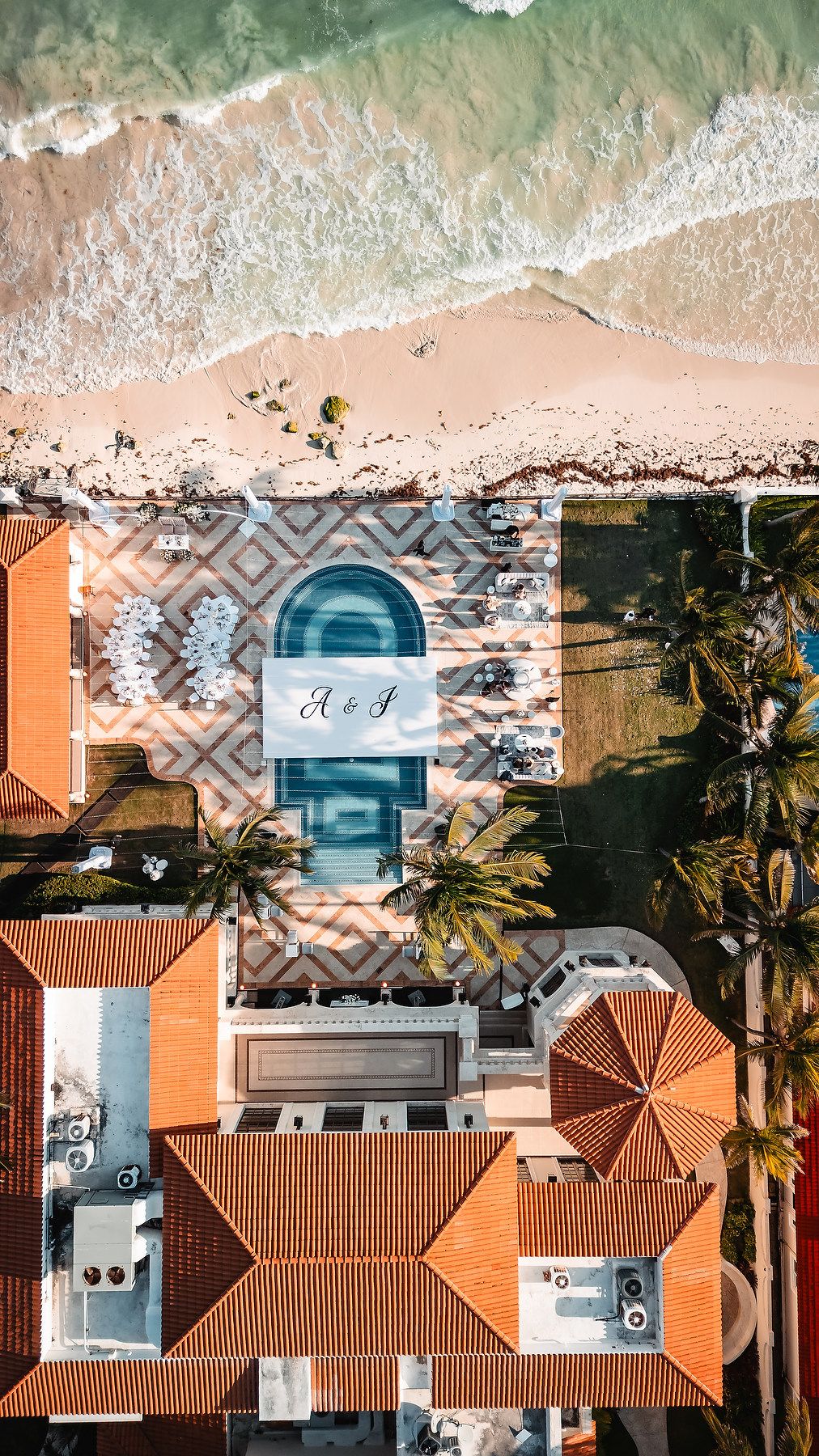 Drone shot of beachfront resort with terracotta roofs and swimming pools along the coastline.