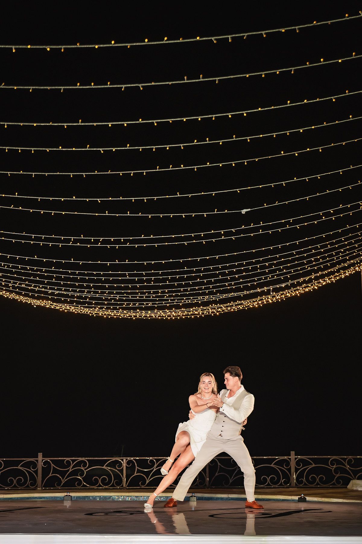 Romantic dance moment under a canopy of twinkling string lights at night.