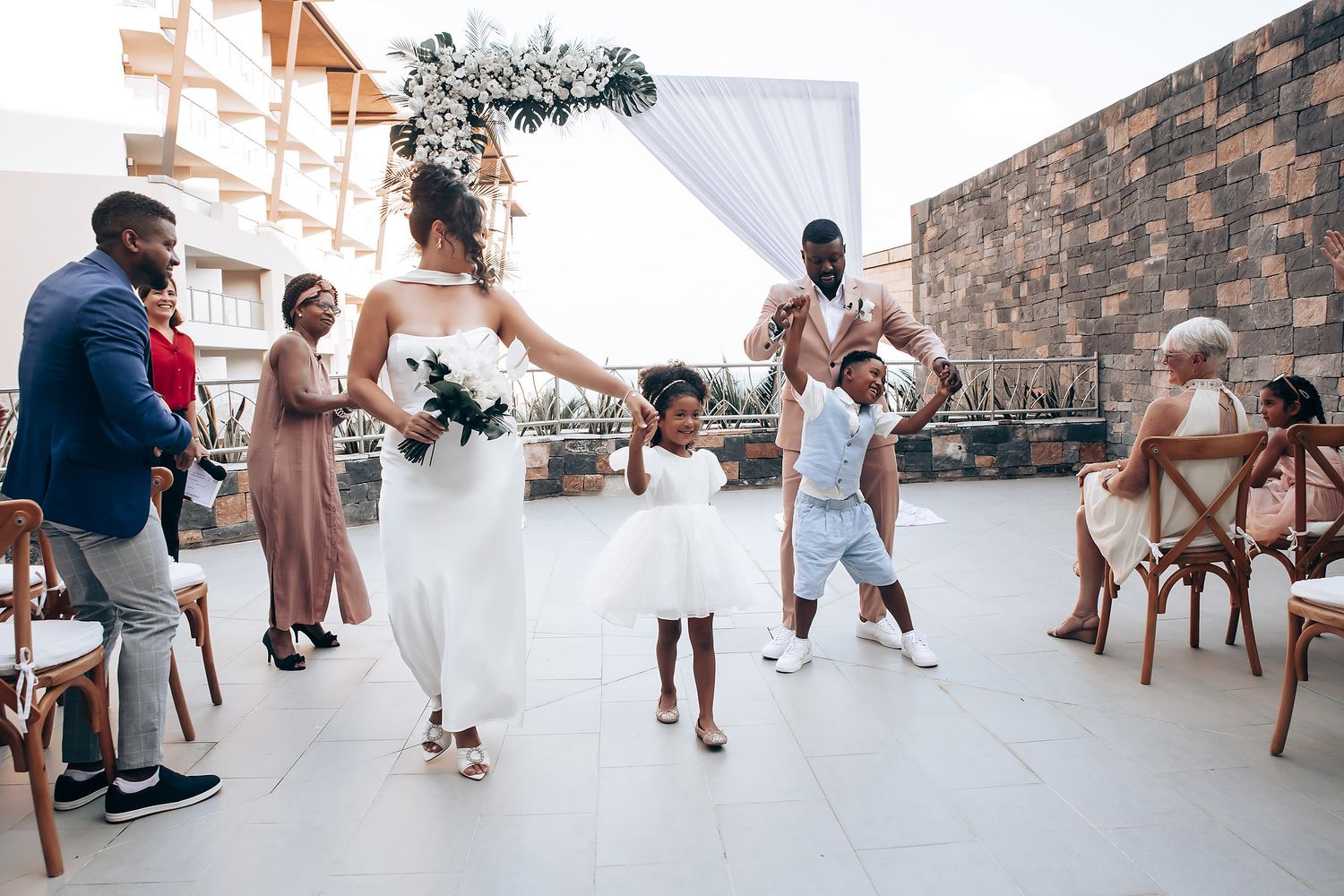 Guests mingle and celebrate at an elegant outdoor reception with stone walls and white decor.